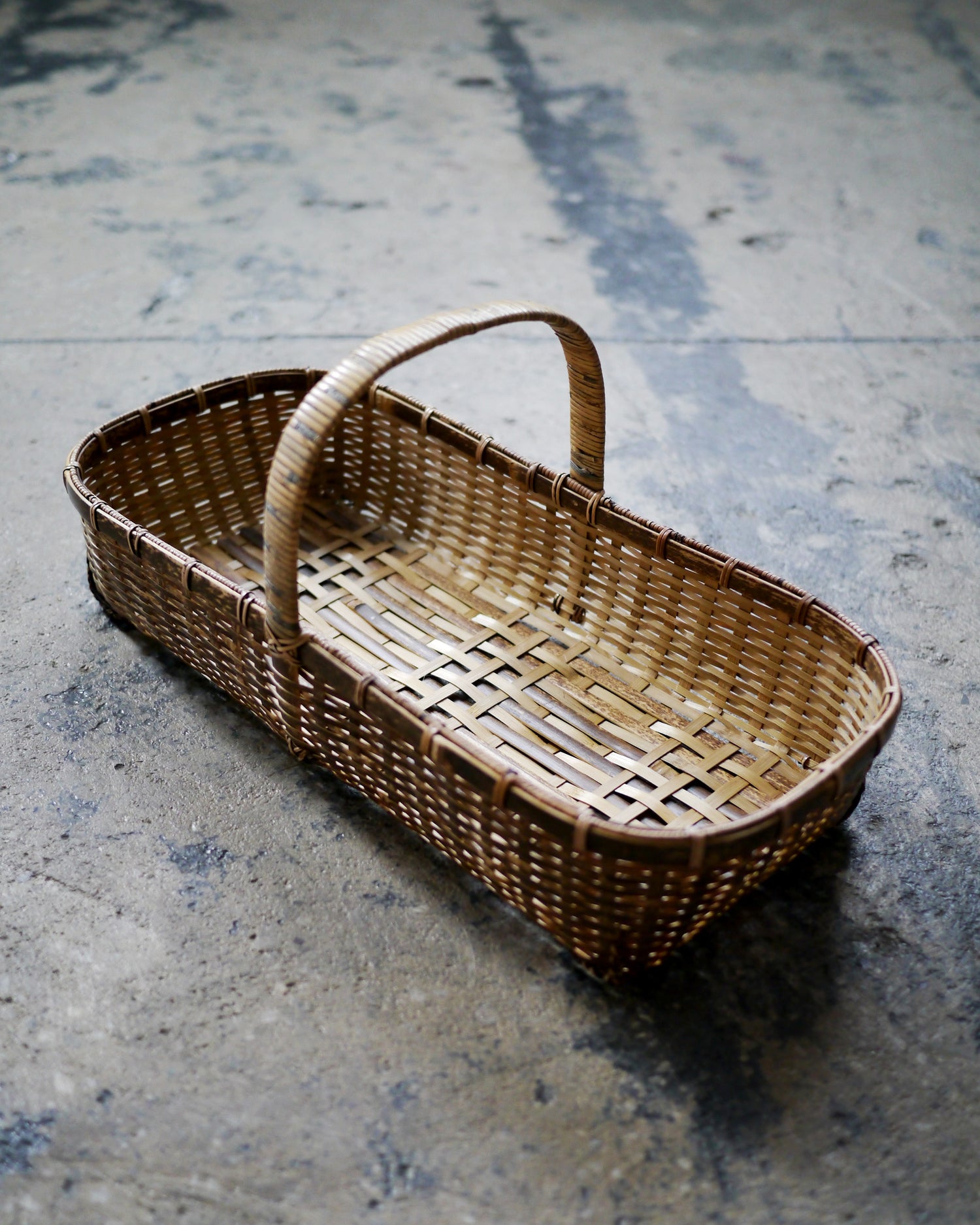 Bird's-eye-view of long toradake bread basket with handle by Kohchosai Kosuga on dark concrete floor.