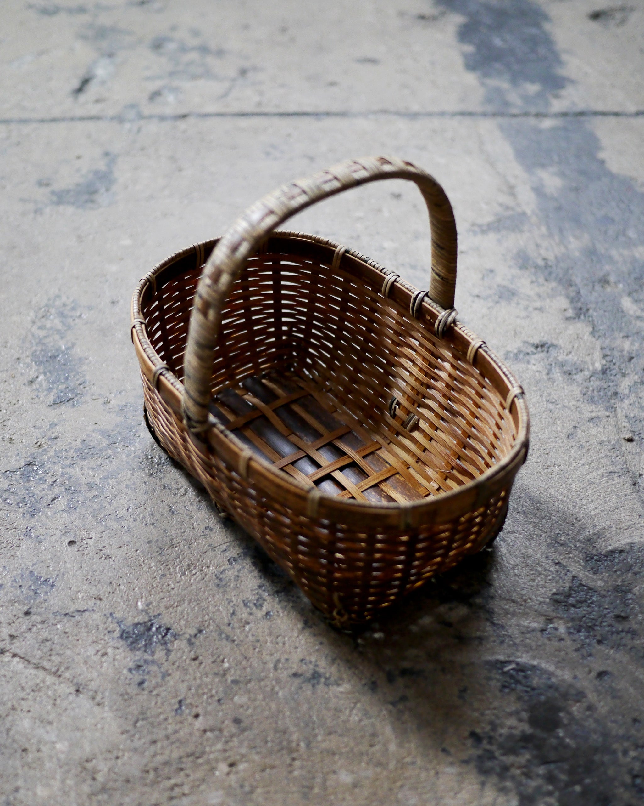Bird's-eye-view of small toradake bread basket with handle by Kohchosai Kosuga on dark concrete floor.