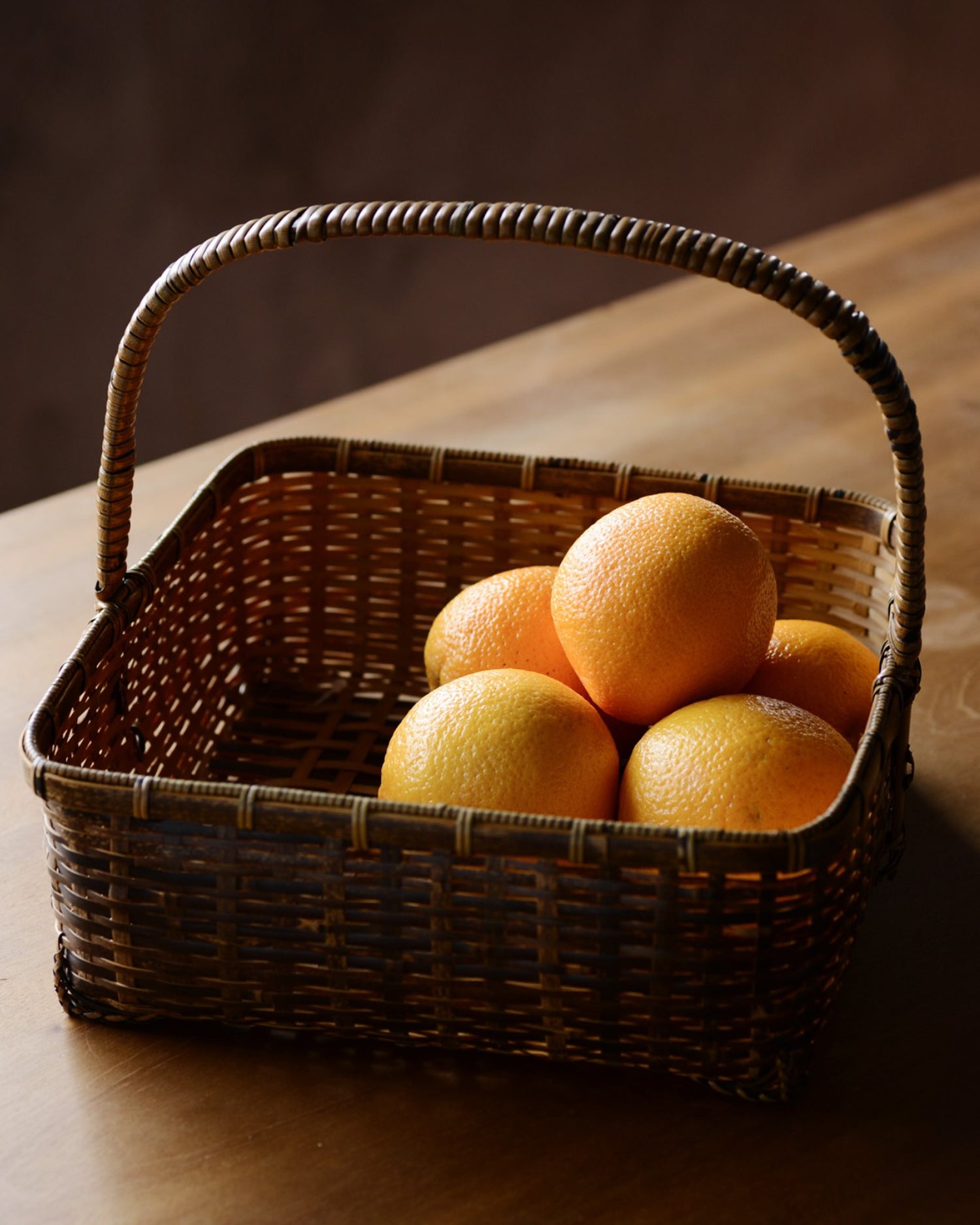 In situation image of square toradake bread basket with oranges on a wood surface.
