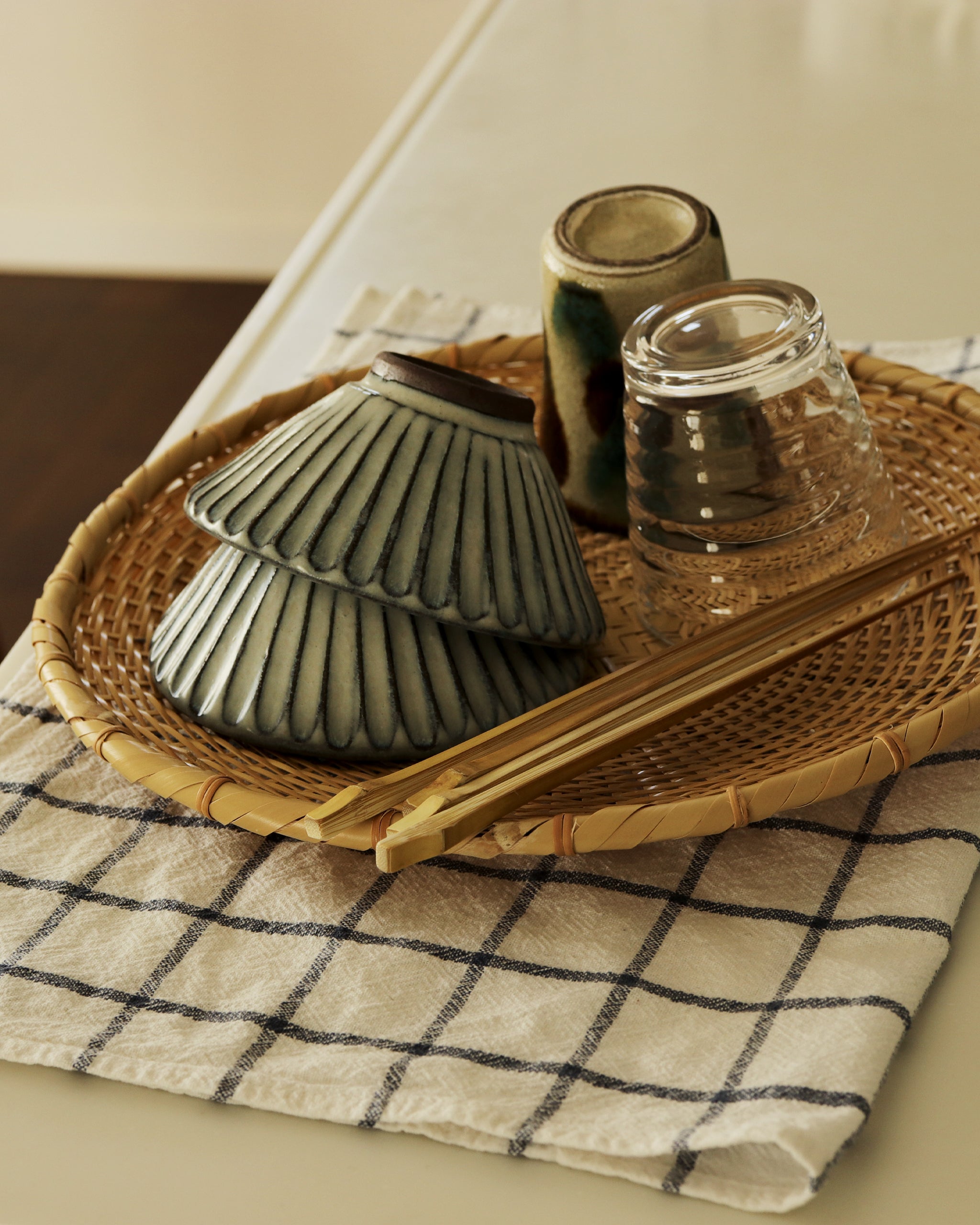 Round low tray sitting on top of a grided kitchen towel. Two cups, two bowls, and two pairs of chopsticks sit in the tray.