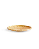 Round low plate-like tray made out of natural colored woven bamboo. It sits against white background.