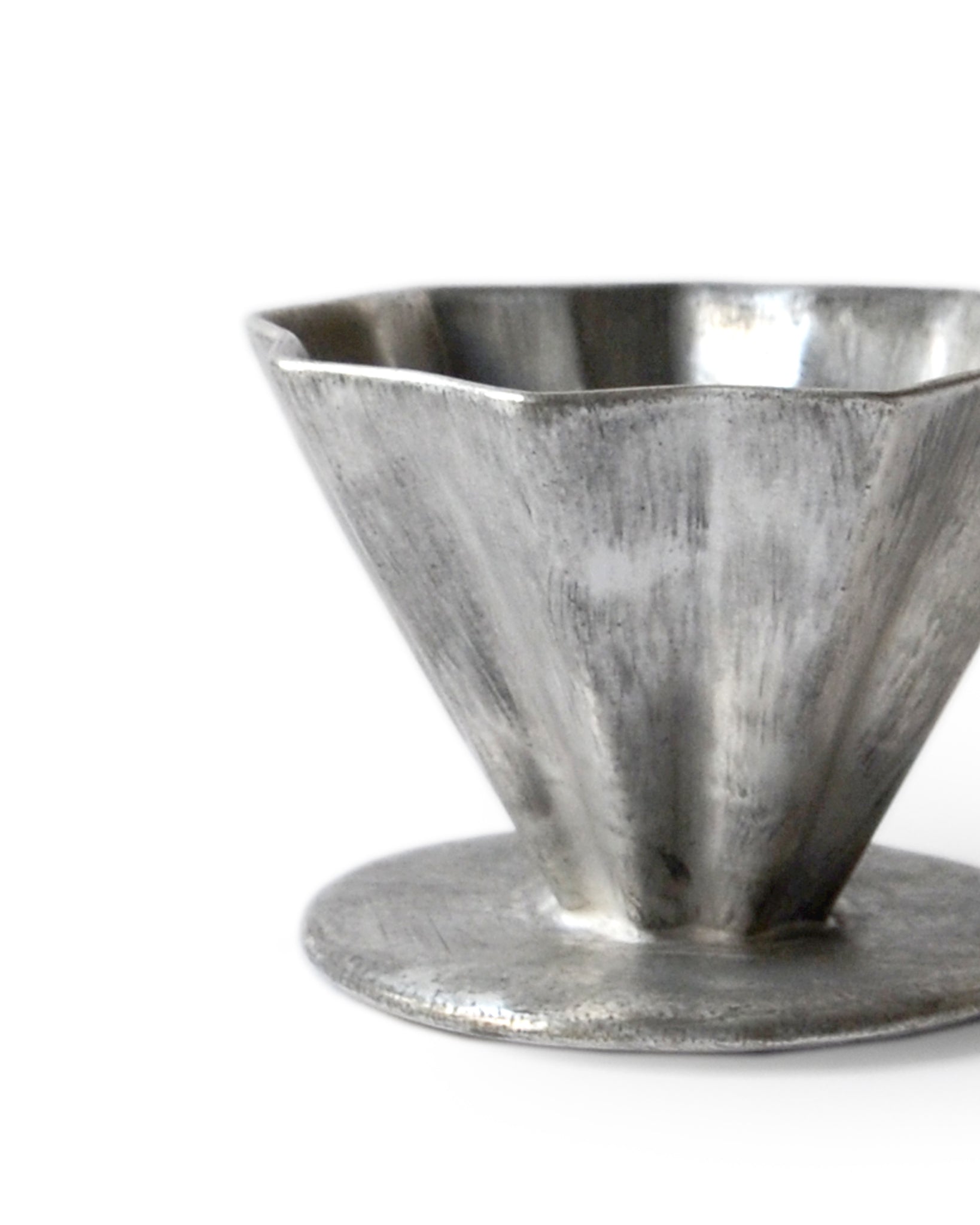 Detail view of the silver glazed coffee dripper silhouetted against white background.