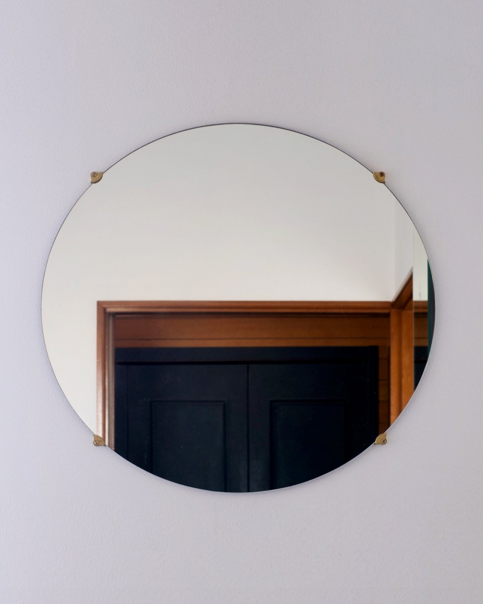 Round mirror installed on the wall with four matureware mirror stoppers. Black and brown wood door is reflected in the mirror.