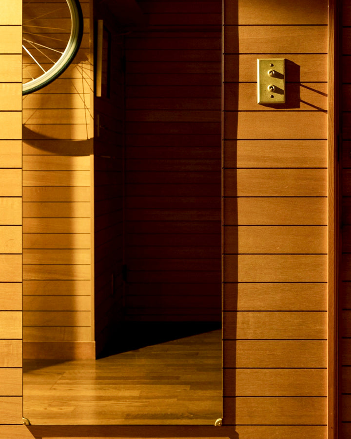 Cropped long rectangular mirror installed with matureware mirror stopped on its corners. Matureware switch plate is on the wall next to the mirror in an all wood room. 