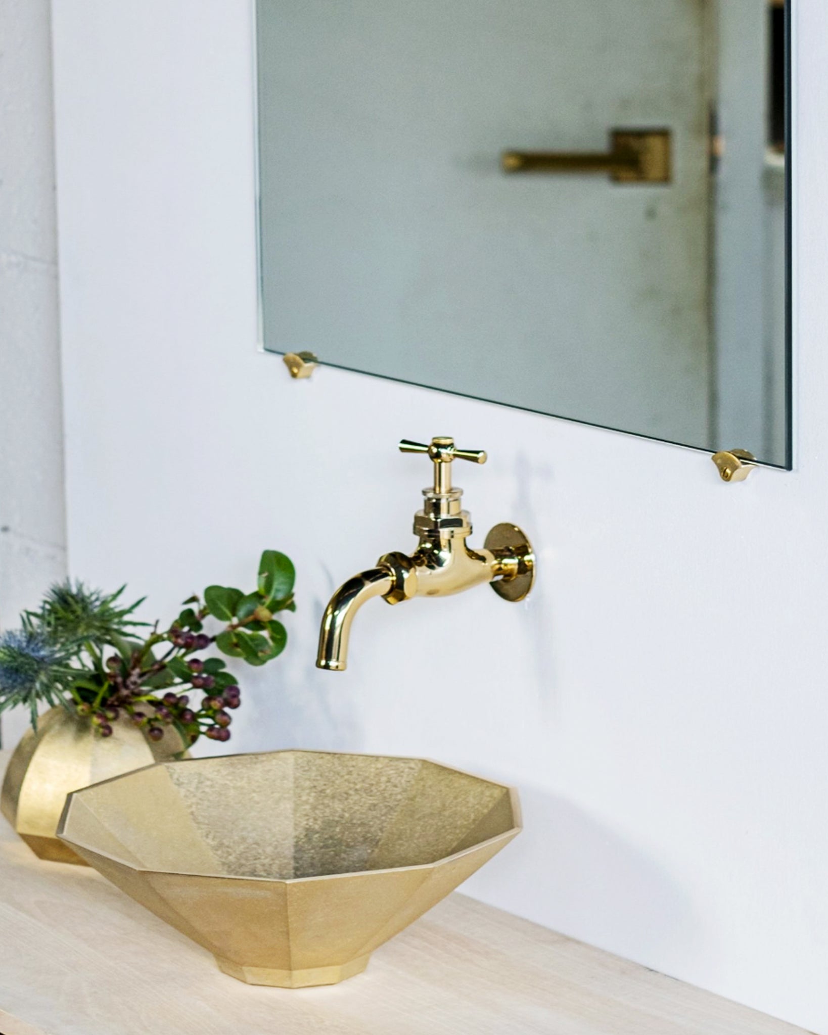 Matureware bath items installed in a space featuring wash bowl, facet, vase, and mirror stoppers. Matureware lever and handle on a door is also reflected through the mirror.