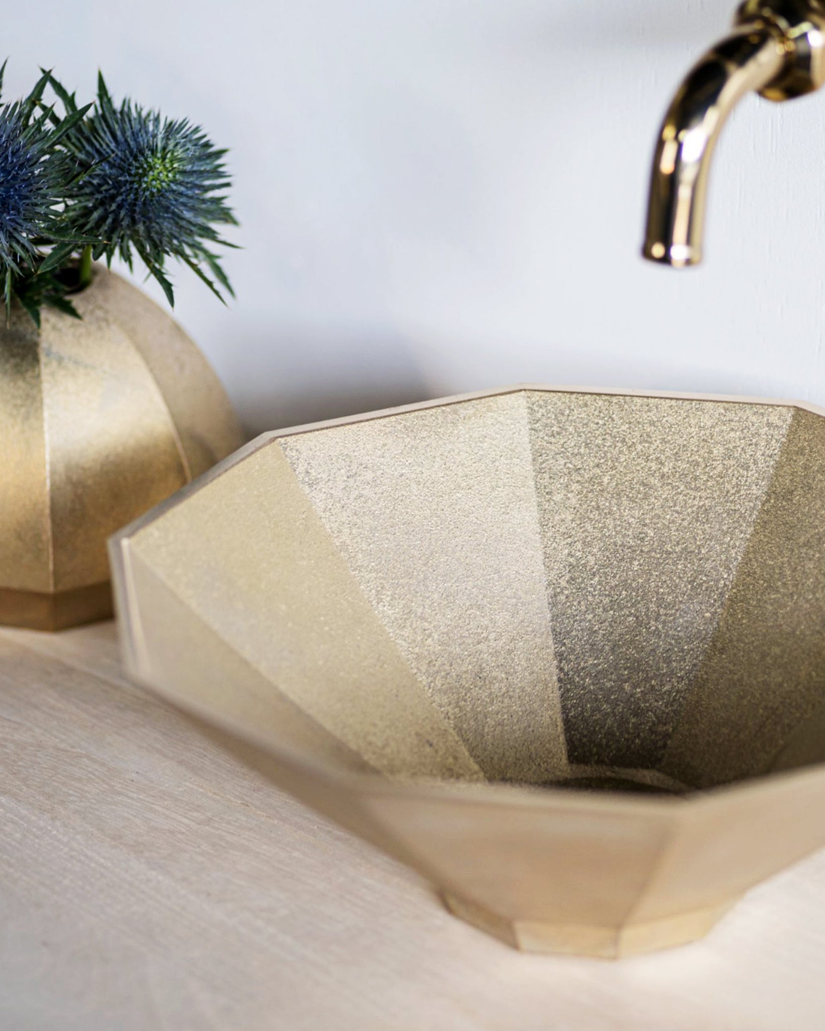 Matureware wash bowl installed on a oak wood countertop. Brass vase with blue flowers in it is placed next to the wash bowl.