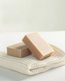 Two bars of Mutenka Sekken soap One leans on top of the other. They both sit atop of a white folded waffle towel.