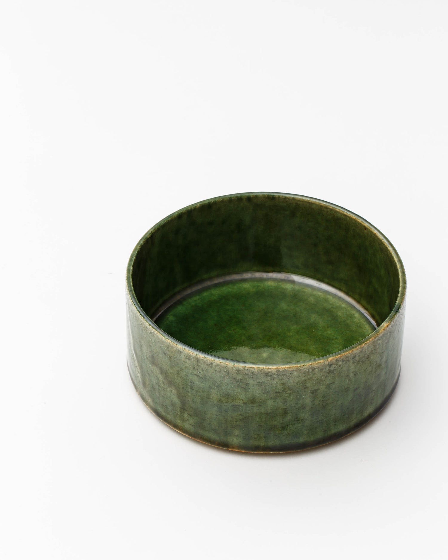 Image looking into small ceramic oribe bowl with deep green glaze by Time and Style against white-gray background.