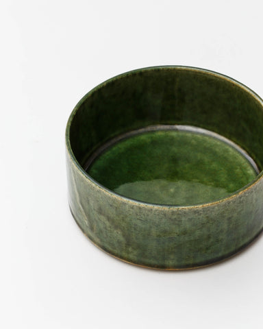 Cropped image looking into small ceramic oribe bowl with deep green glaze by Time and Style against white-gray background.