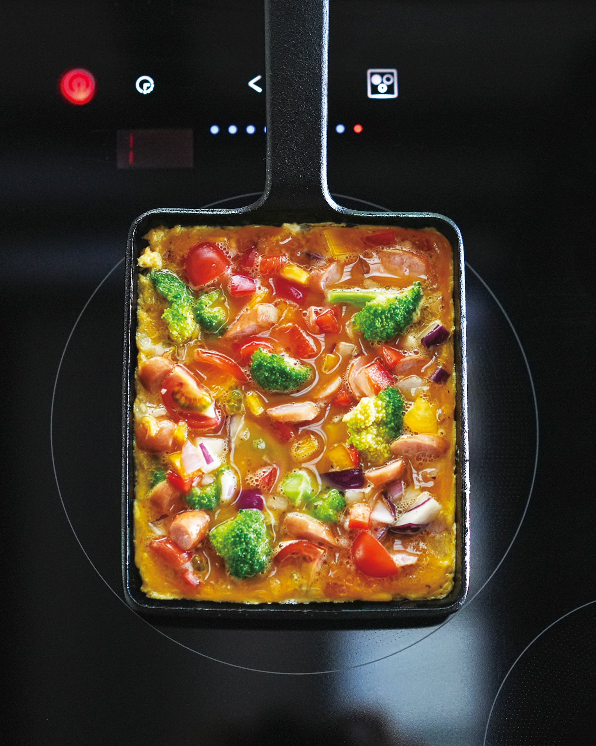 Vegetable and seafood omelet in a cast iron rectangular pan on a black stovetop
