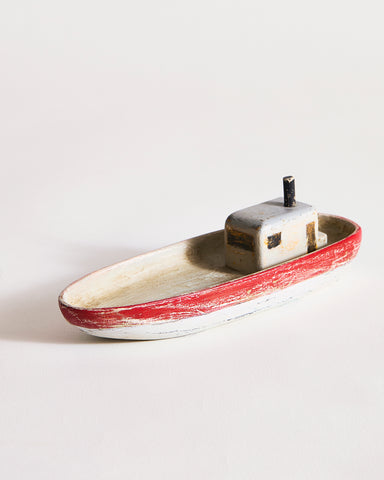 Small wooden boat with red,gray, and black paint by Ryuji Mitani on a light gray background