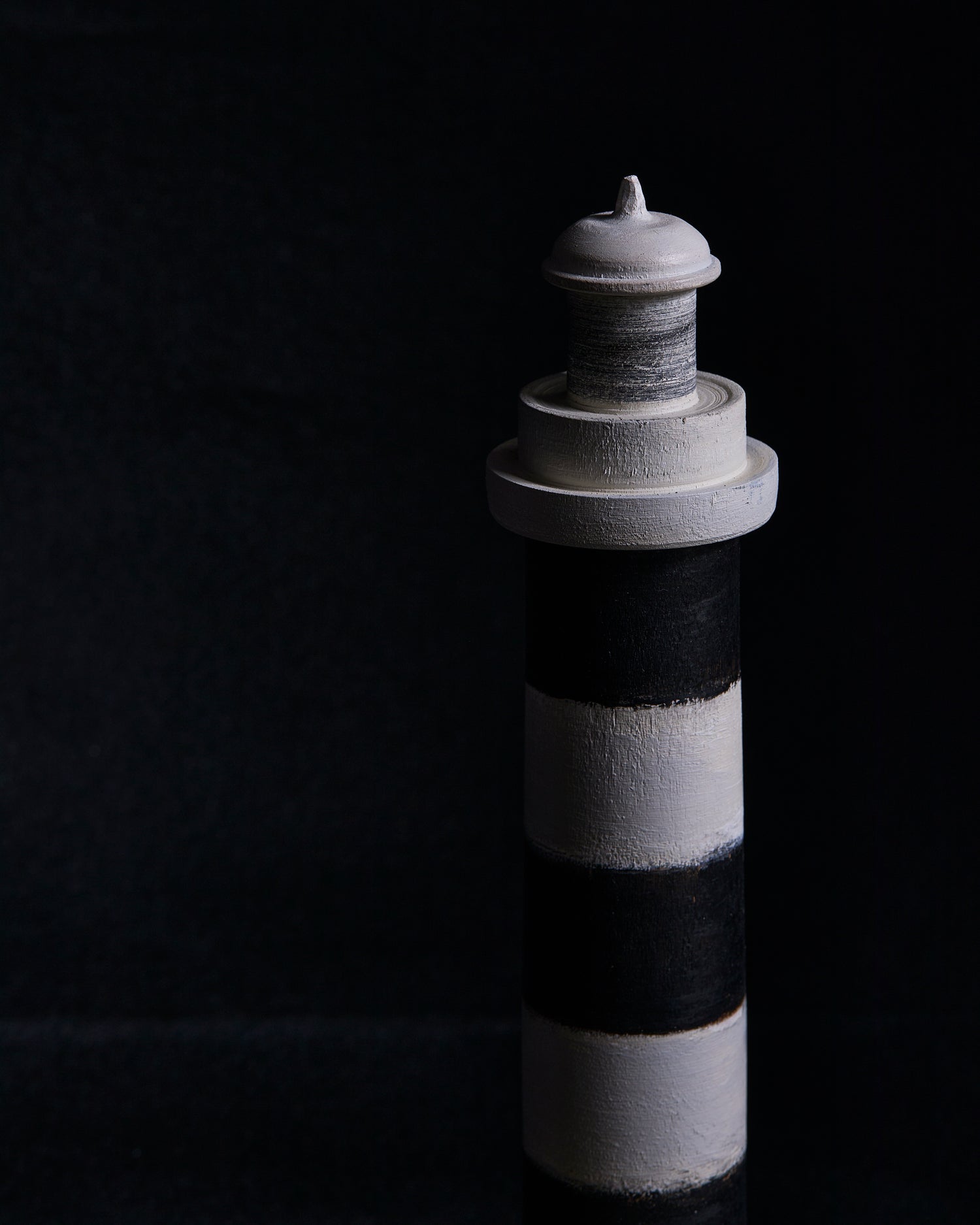 The top point of a black and gray striped lighthouse sculpture by Ryuji Mitani on a black background