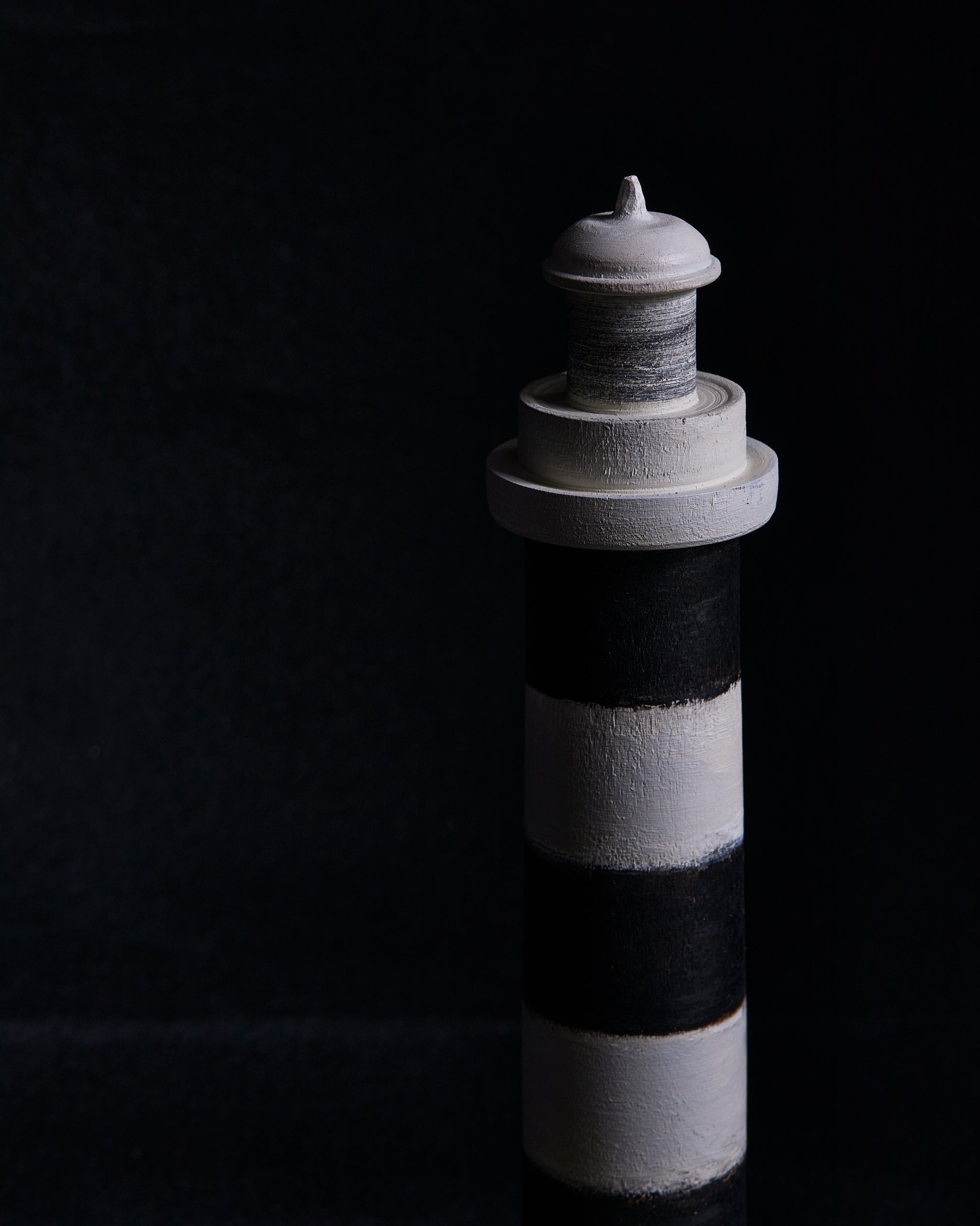 The top point of a black and gray striped lighthouse sculpture by Ryuji Mitani on a black background