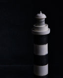 The top point of a black and gray striped lighthouse sculpture by Ryuji Mitani on a black background