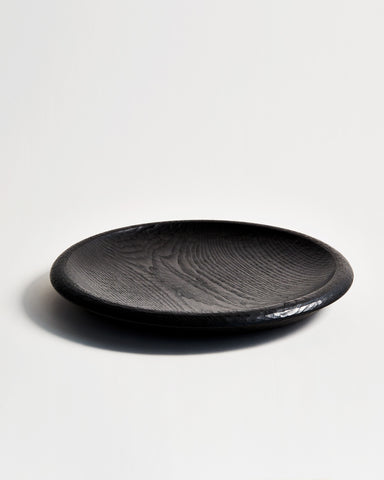 Front view of Noir Round Curved Rim Platter by Ryuji Mitani against white-gray background.