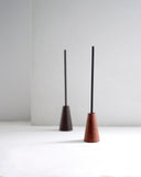 Two wooden cone-shaped incense holders by Ryuji Mitani with black incense on a white background