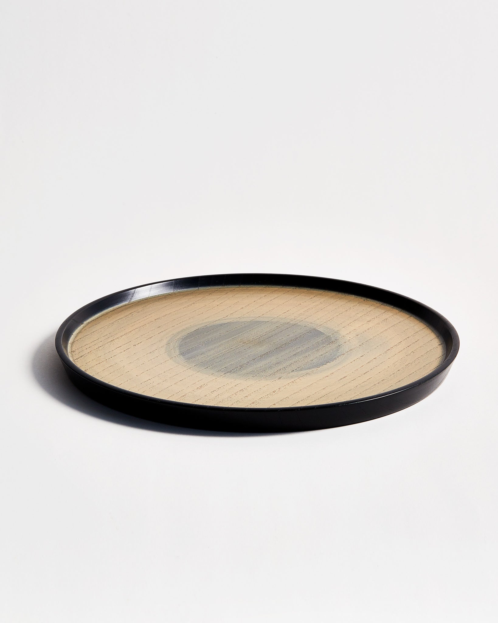 Angled side view of Usuzumi Round Oak Tray by Ryuji Mitani against white-gray background. 