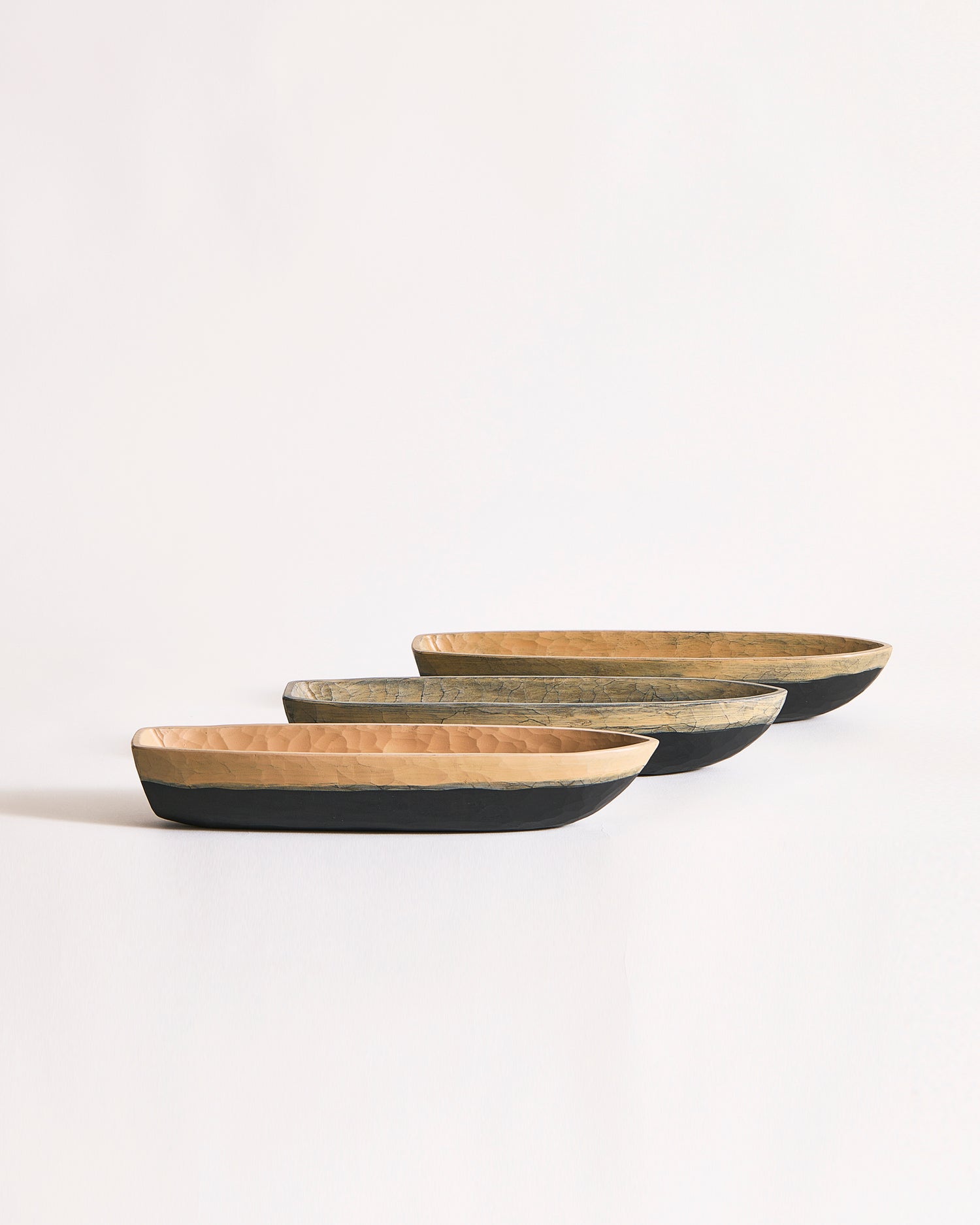 Set of three wooden boat bowls in beige and black on a gray background
