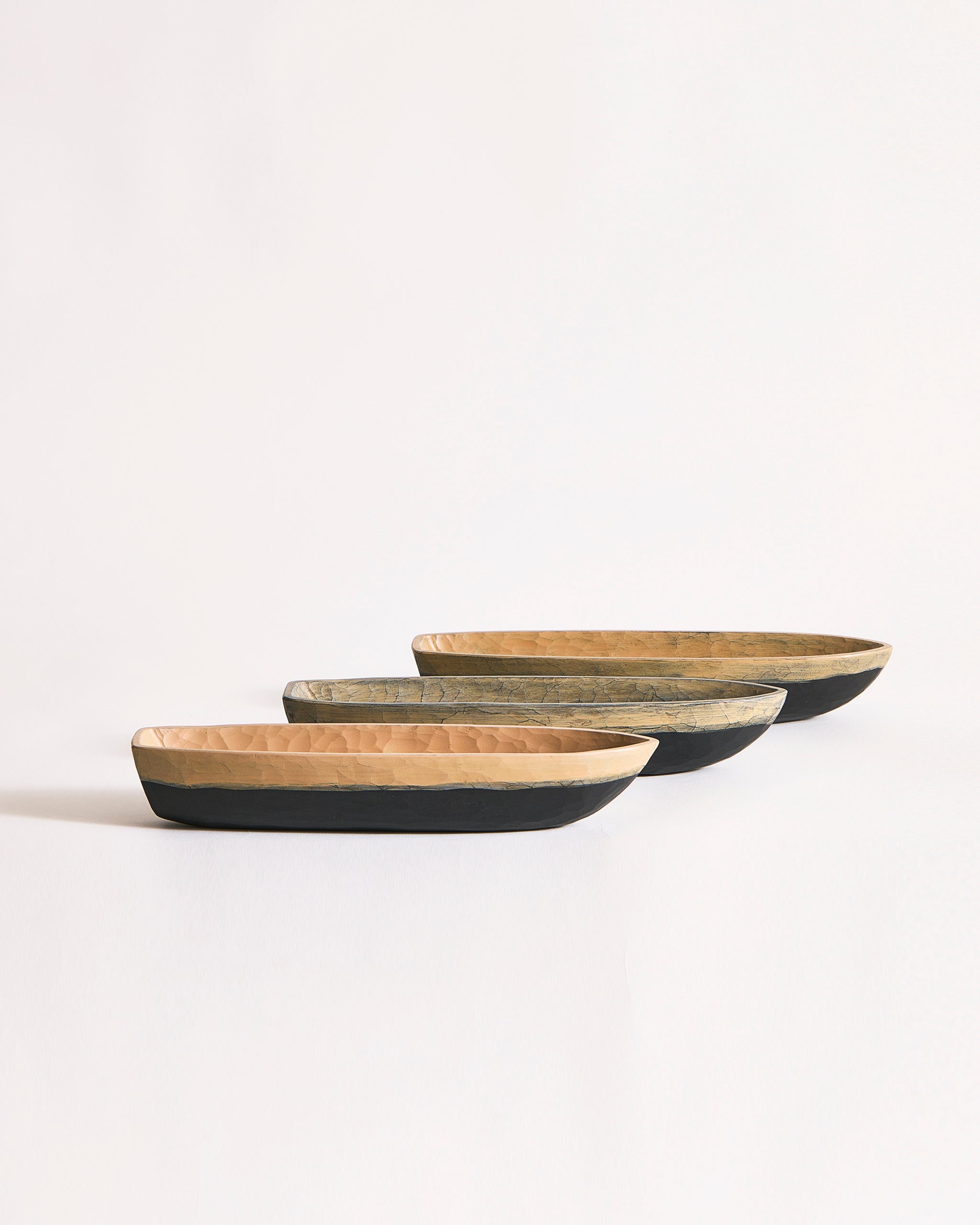 Set of three wooden boat bowls in beige and black on a gray background