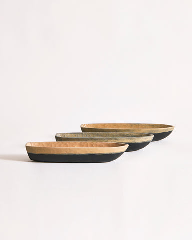Set of three wooden boat bowls in beige and black on a gray background