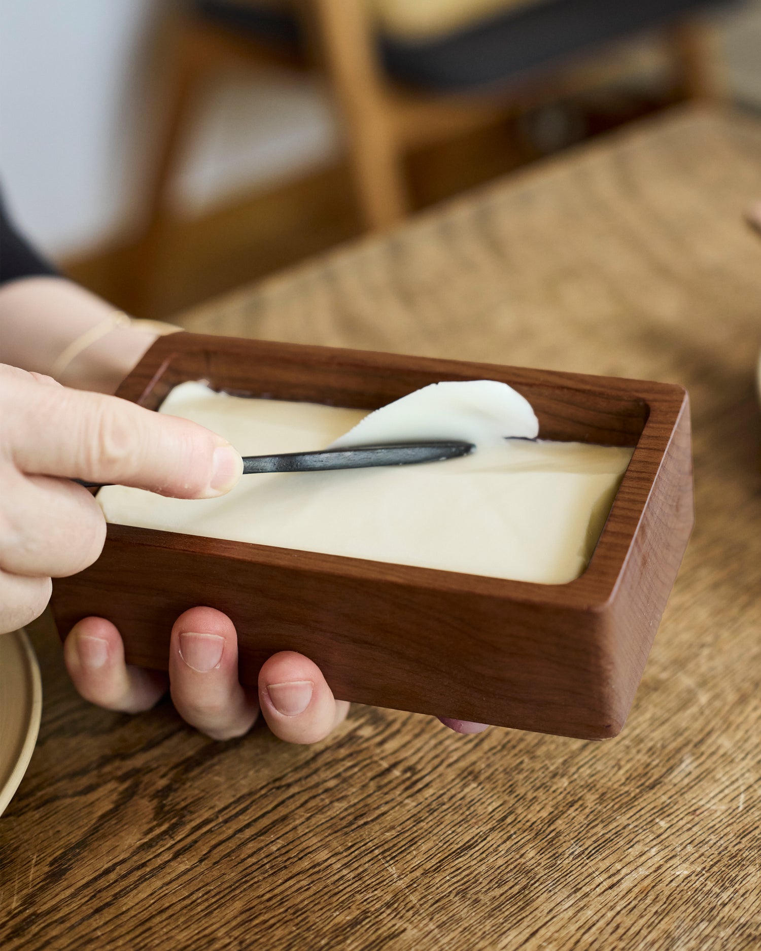 Hand holding a wooden butter box scraping butter with a knife 