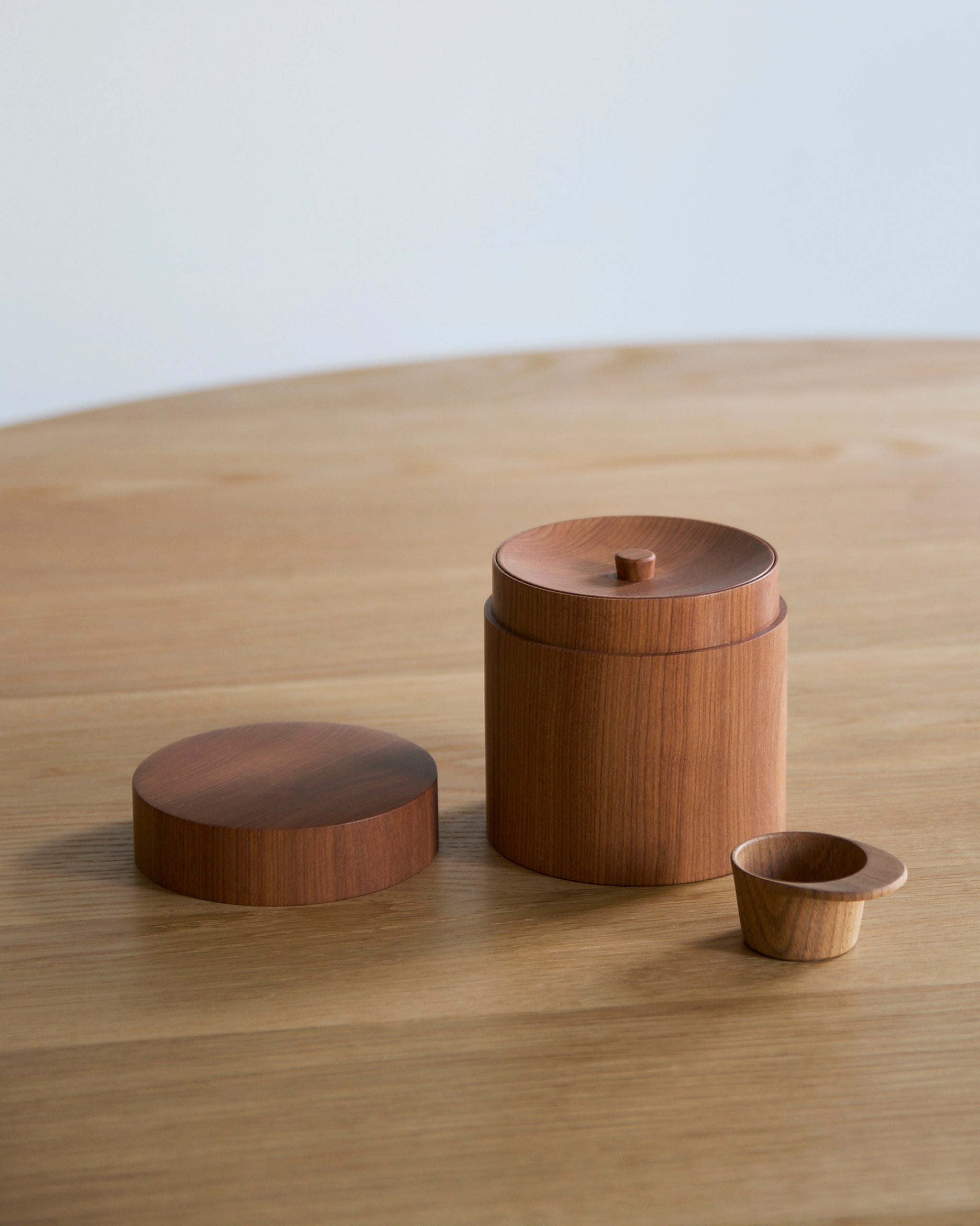 Wooden coffee container with two lids and scoop by Ryuji Mitani on a wooden surface with a plain background