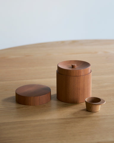 Wooden coffee container with two lids and scoop by Ryuji Mitani on a wooden surface with a plain background