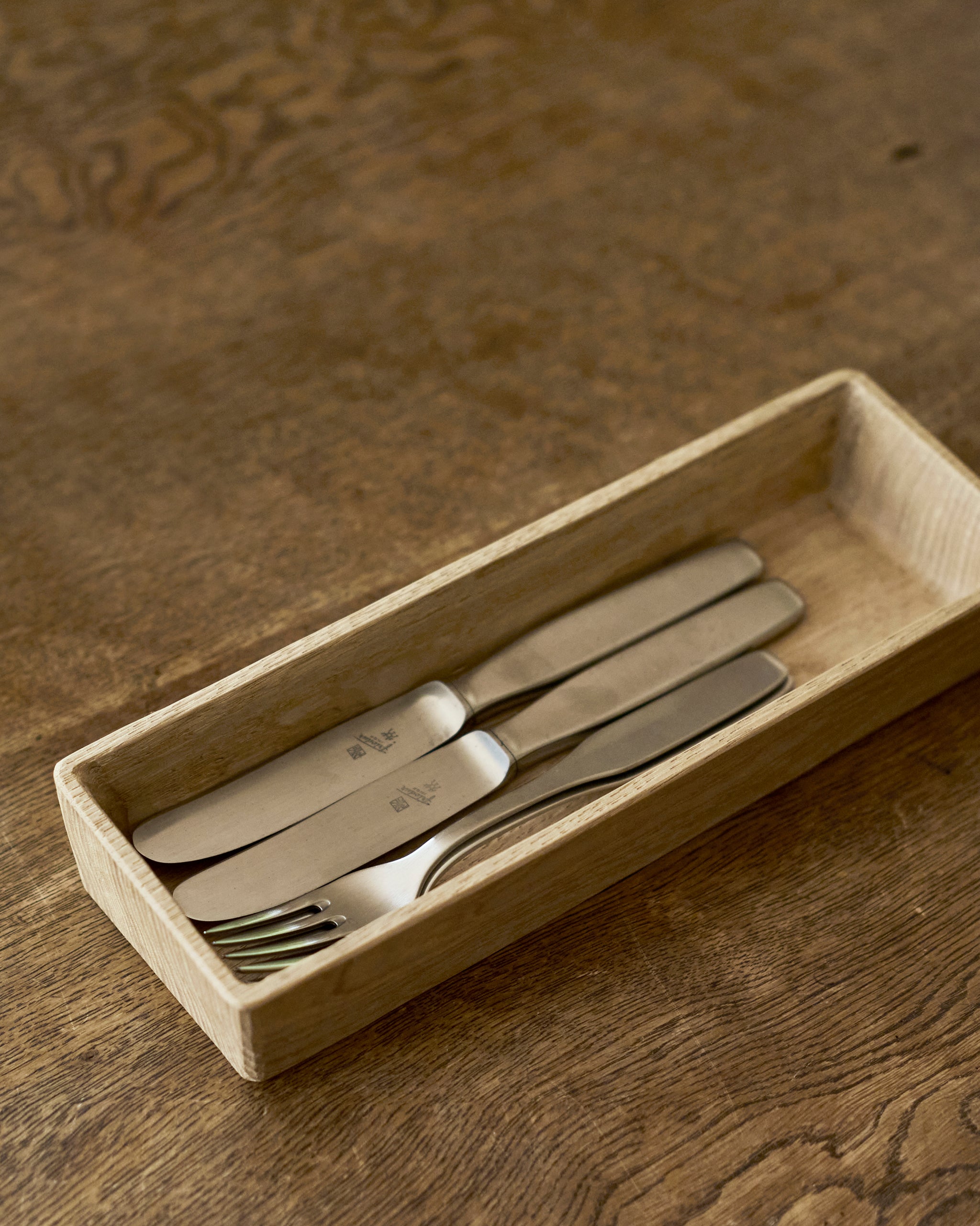 Set of silver cutlery in a wooden tray by Ryuji Mitani on a wooden surface