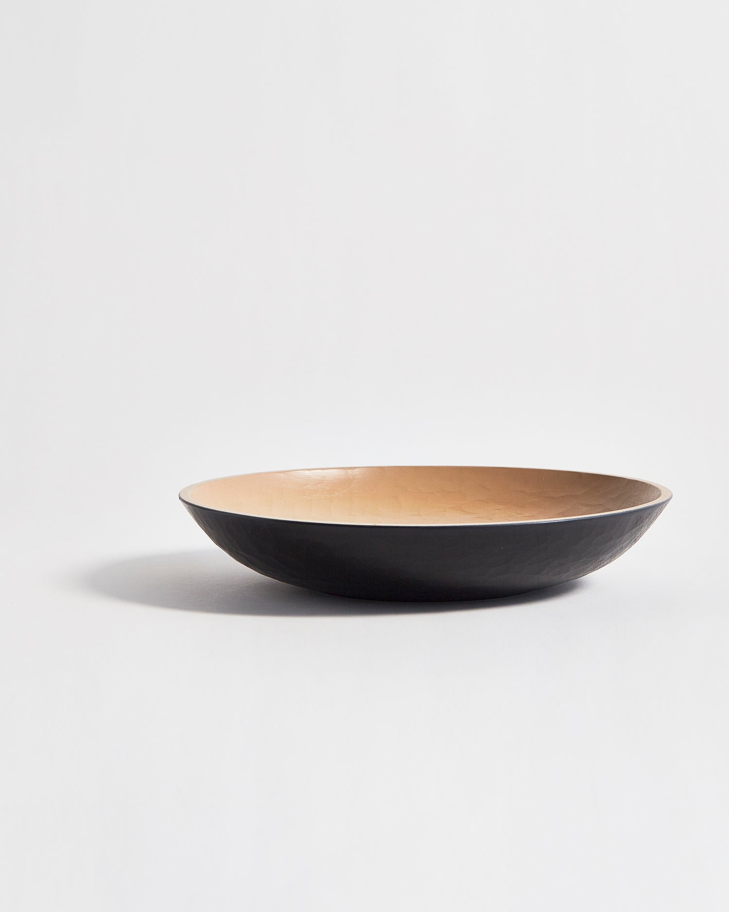 Side view of wooden bowl with beige interior and a black exterior by Ryuji Mitani on a light gray background