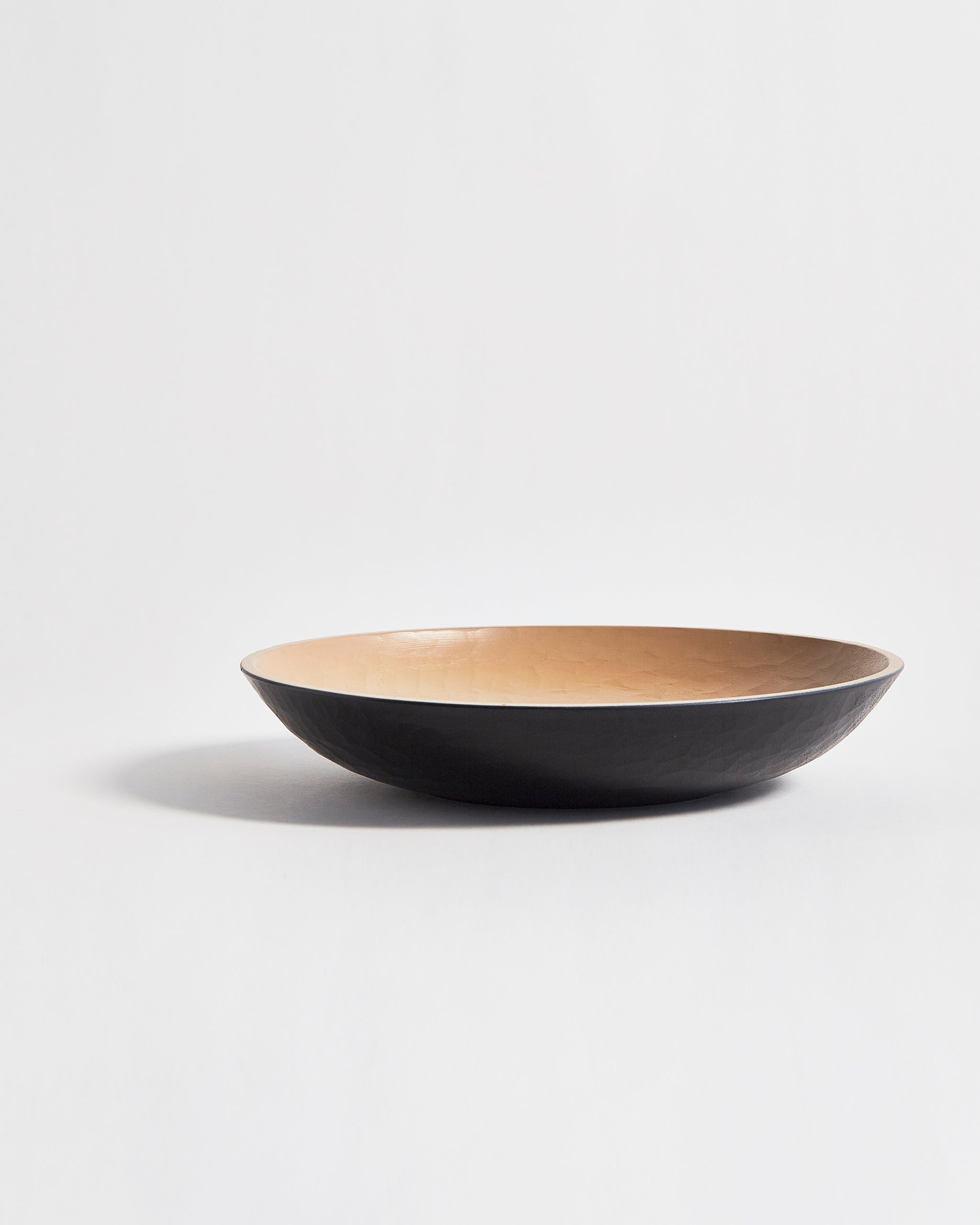 Side view of wooden bowl with beige interior and a black exterior by Ryuji Mitani on a light gray background