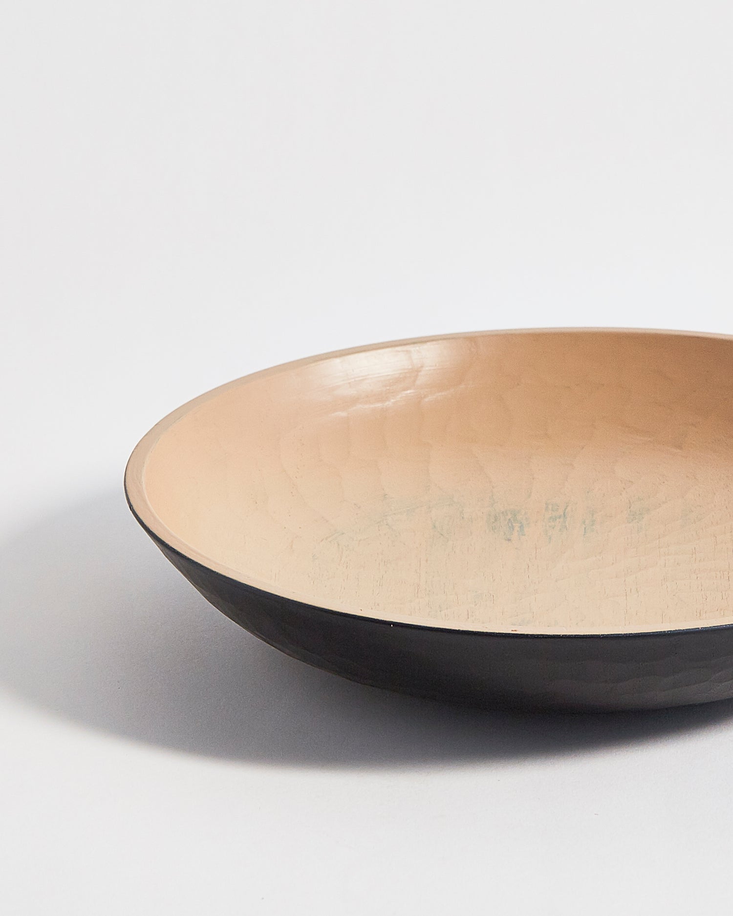 Up-close left corner view of wooden bowl with beige interior and a black exterior by Ryuji Mitani on a light gray background