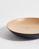 Up-close left corner view of wooden bowl with beige interior and a black exterior by Ryuji Mitani on a light gray background
