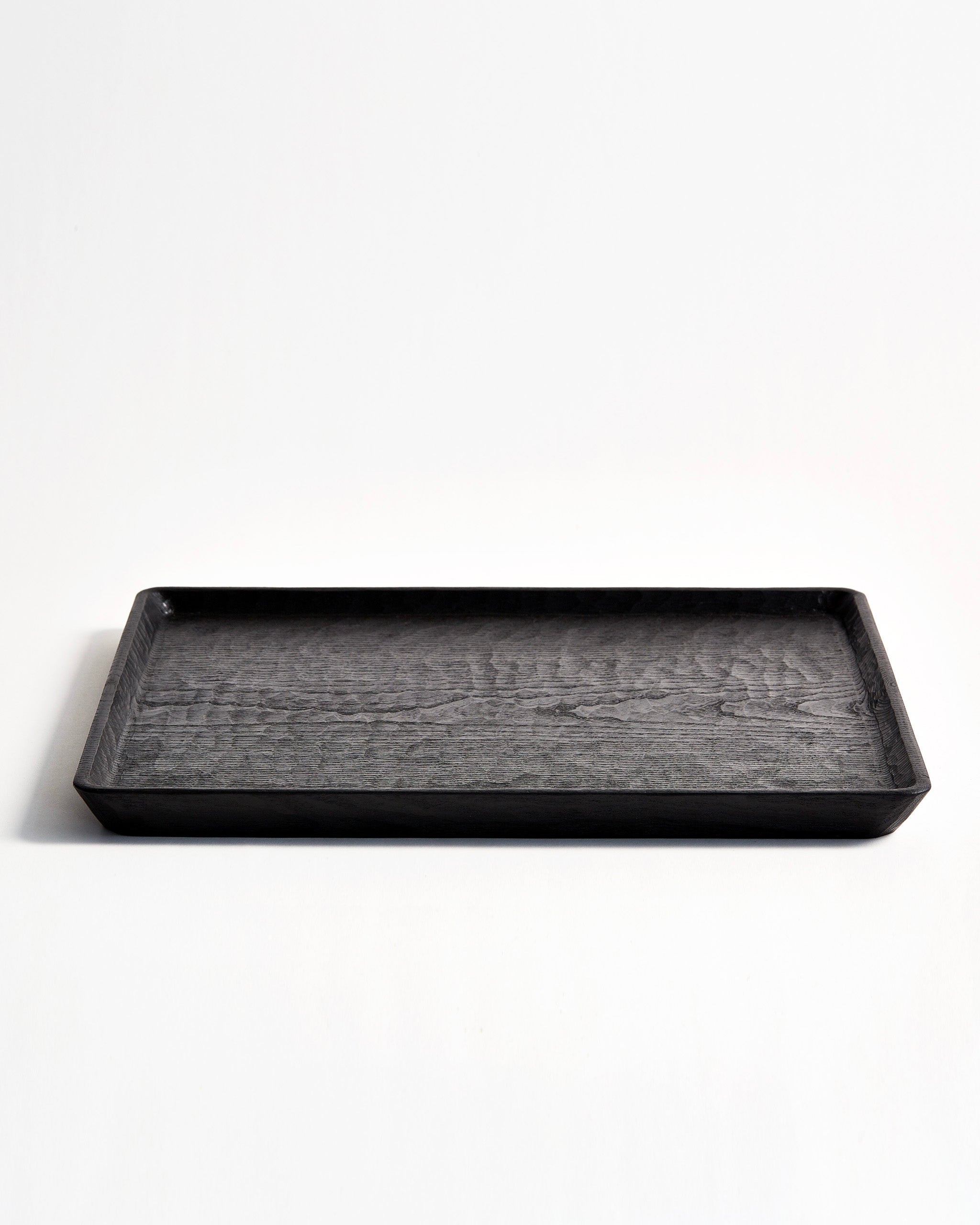 Front view of Carved Noir Wood Tray with Enju Wood by Ryuji Mitani against white-gray background.