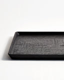Cropped view of Carved Noir Wood Tray with Enju Wood by Ryuji Mitani against white-gray background. 