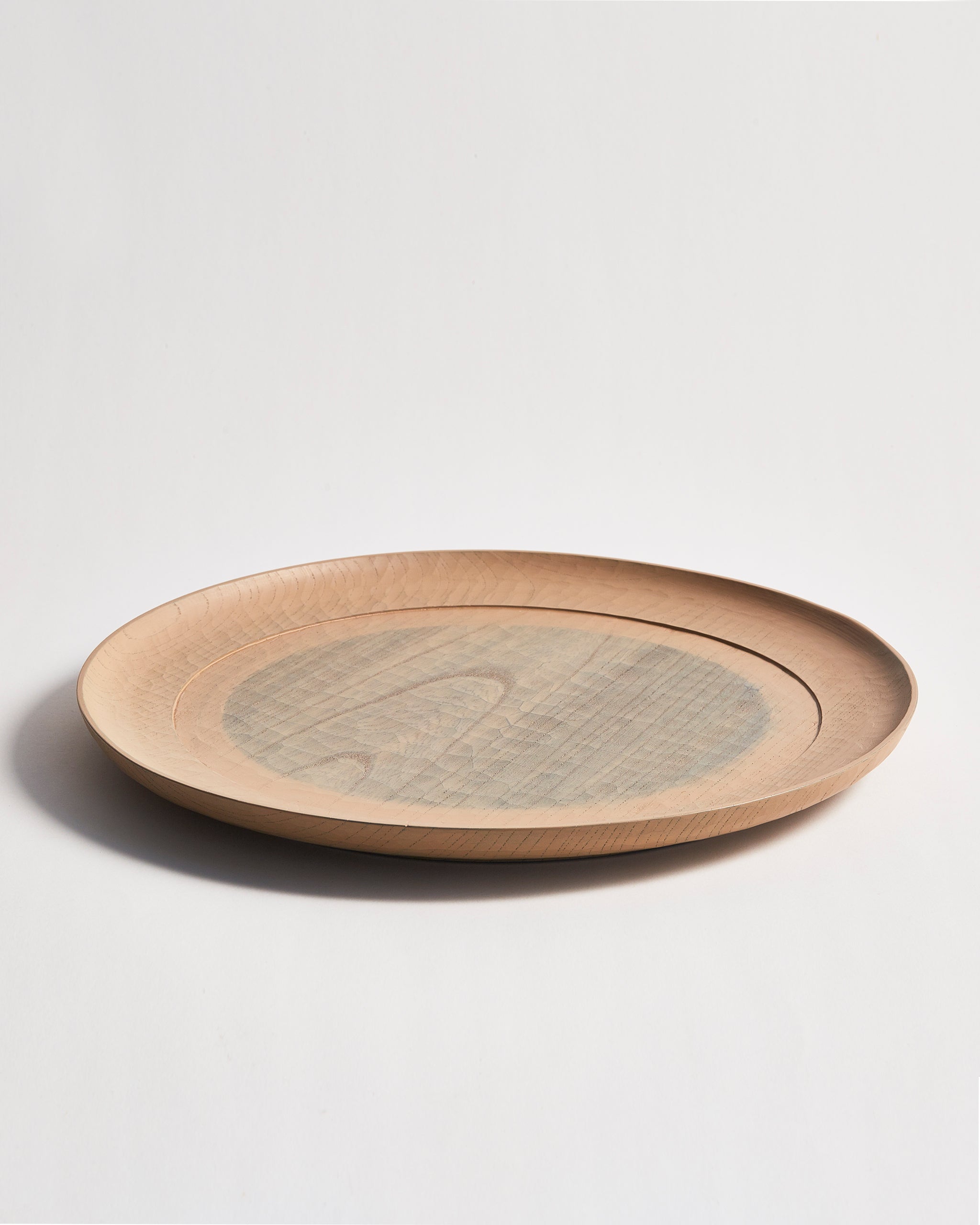 Side view of a round beige wooden plate with a gray circle center by Ryuji Mitani on a gray background