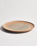 Side view of a round beige wooden plate with a gray circle center by Ryuji Mitani on a gray background
