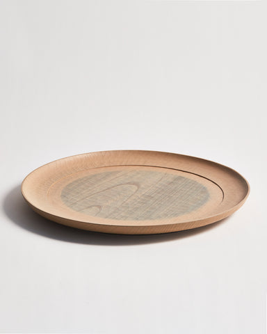 Side view of a round beige wooden plate with a gray circle center by Ryuji Mitani on a gray background