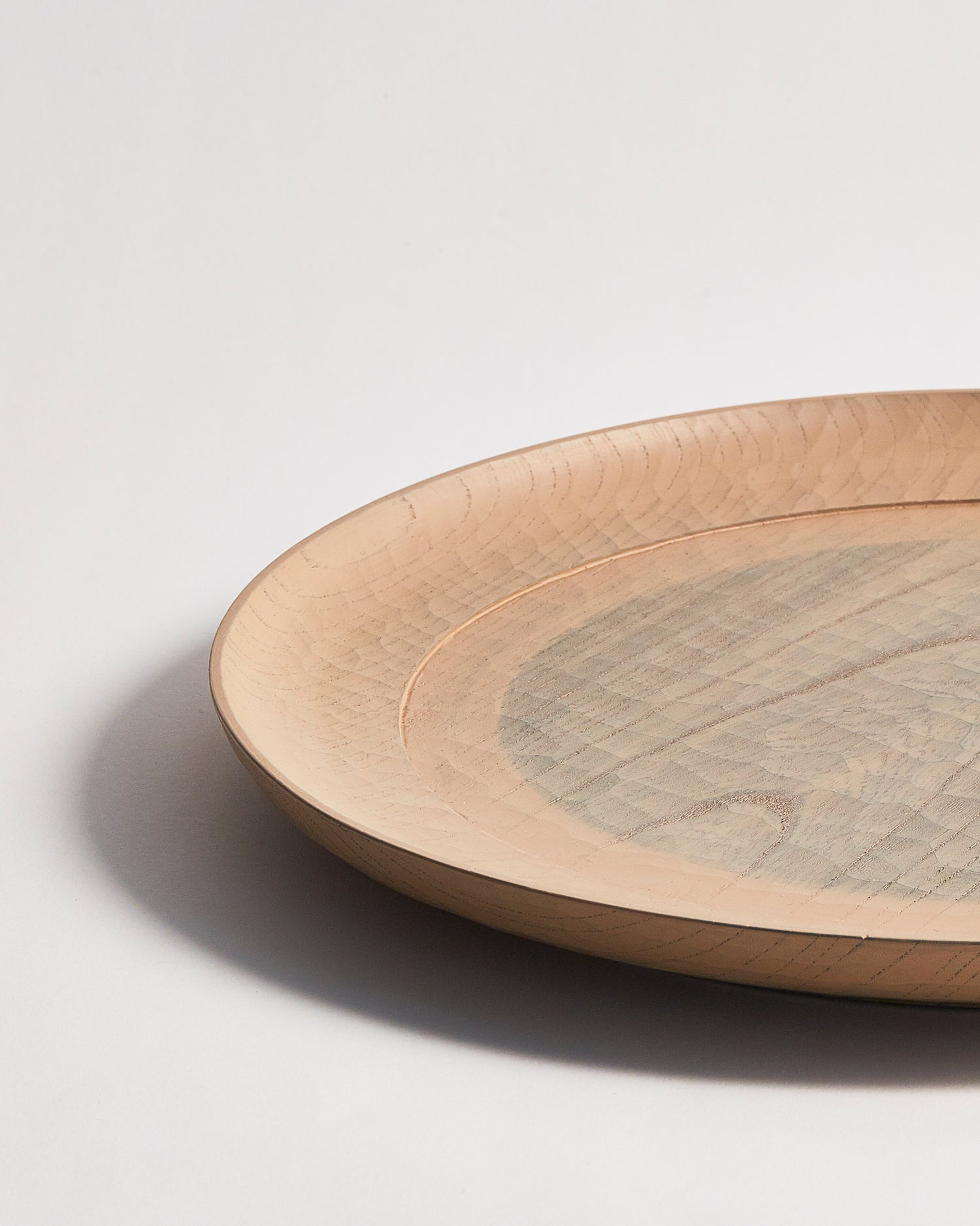 Up-close side profile view of a round beige wooden plate with a gray circle center by Ryuji Mitani on a gray background