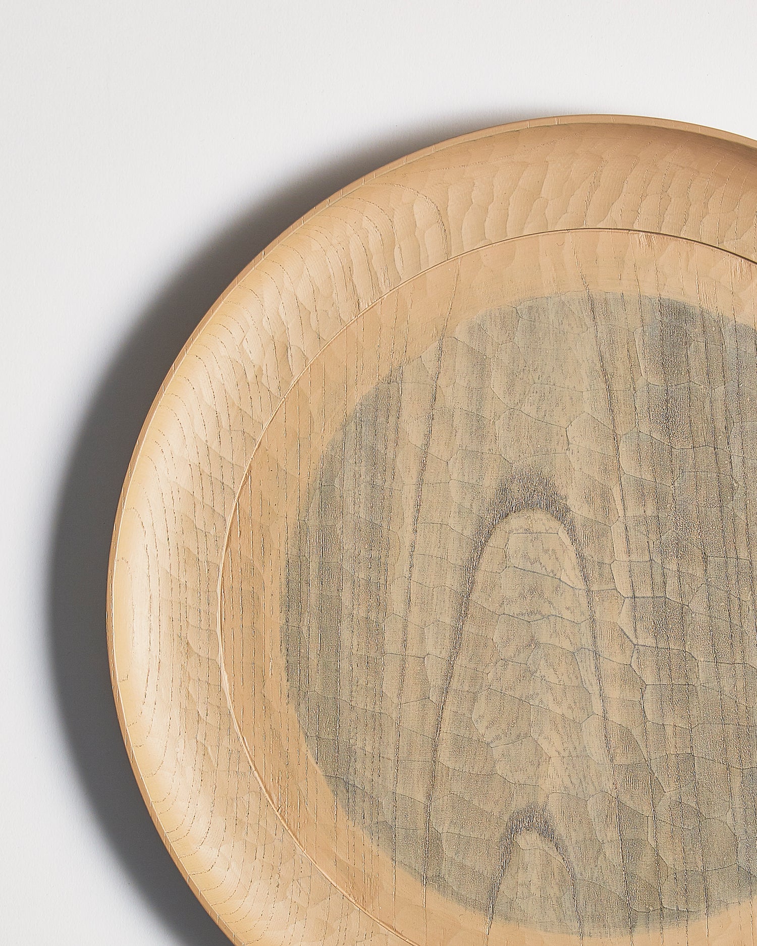 Up-close left corner of a round beige wooden plate with a gray circle center by Ryuji Mitani on a light gray background