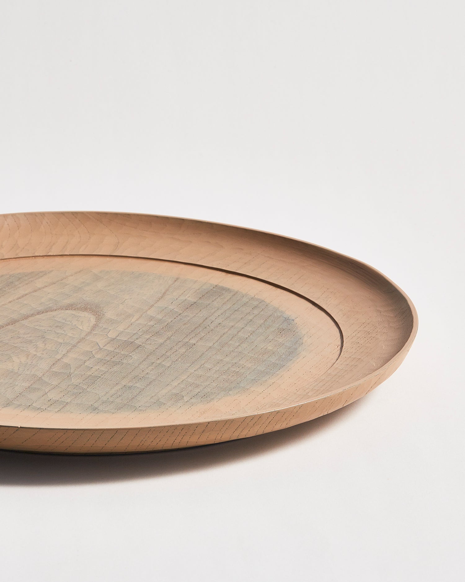 Up-close side profile view of a round beige wooden plate with a gray circle center by Ryuji Mitani on a gray background