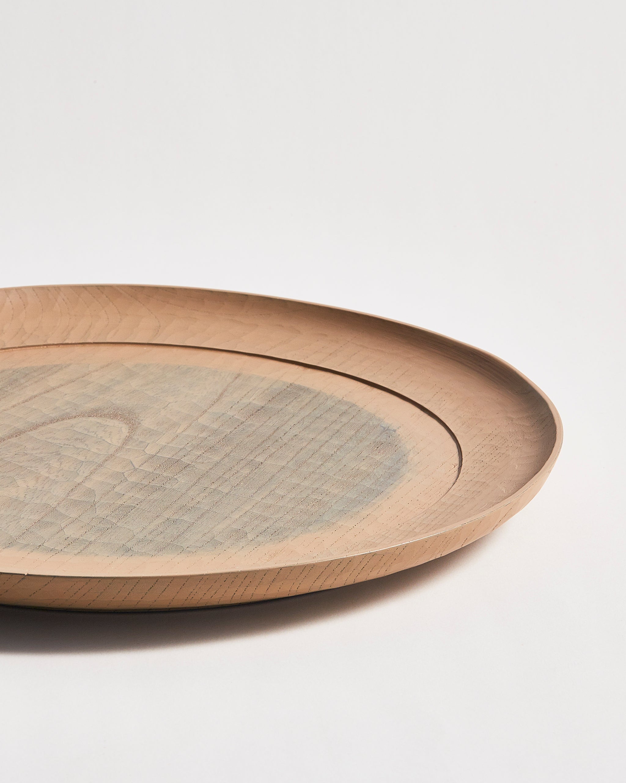 Up-close side profile view of a round beige wooden plate with a gray circle center by Ryuji Mitani on a gray background