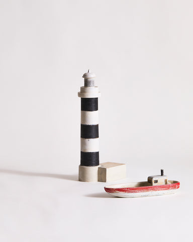 Wooden lighthouse sculpture with black and gray stripes and a wooden boat by Ryuji Mitani on a light gray background