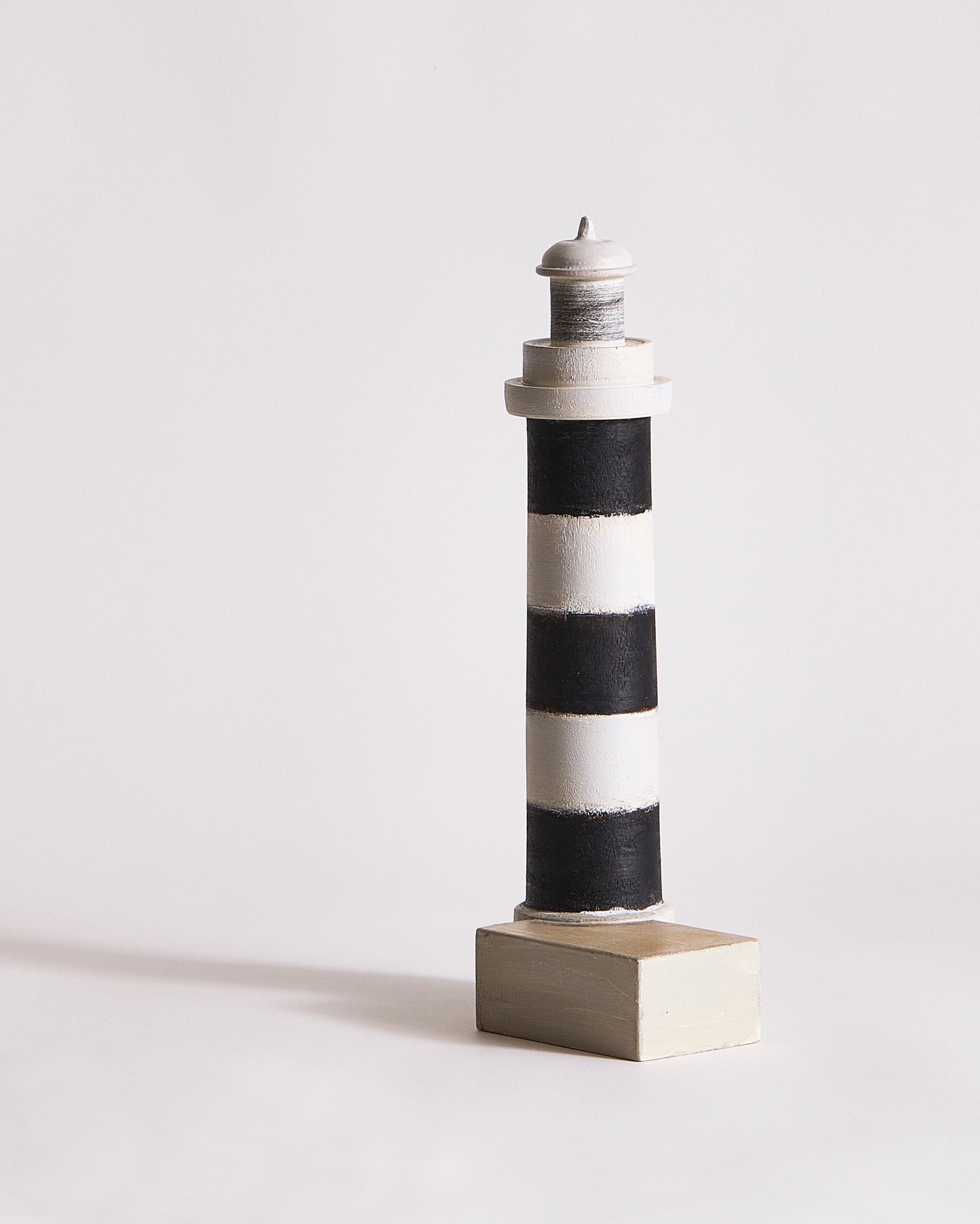 Wooden lighthouse sculpture with black and gray stripes by Ryuji Mitani on a light gray background