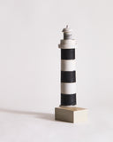 Wooden lighthouse sculpture with black and gray stripes by Ryuji Mitani on a light gray background