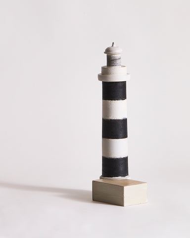 Wooden lighthouse sculpture with black and gray stripes by Ryuji Mitani on a light gray background