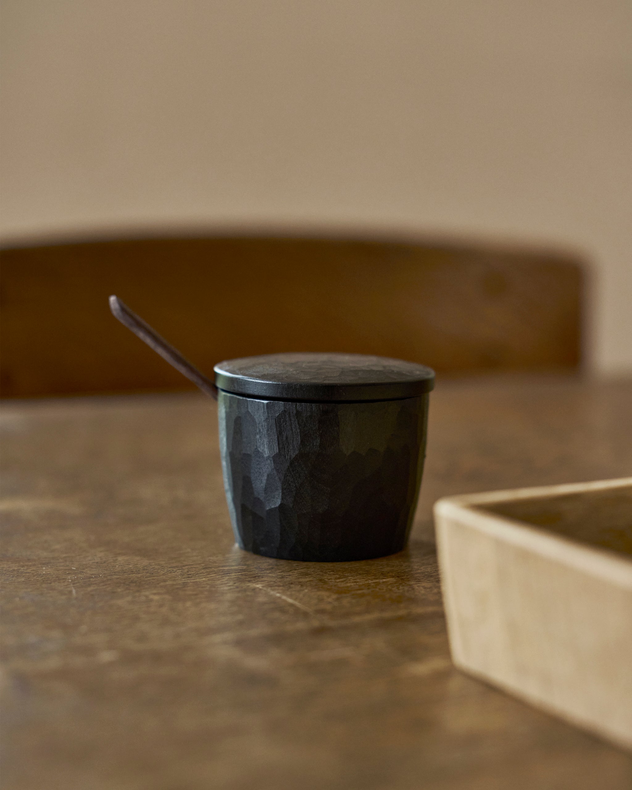 Black wooden container with lid and spoon on a wooden surface