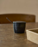 Black wooden container with lid and spoon on a wooden surface