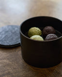 Opened wooden two-tiered box by Ryuji Mitani with green and purple spherical treats on a wooden surface