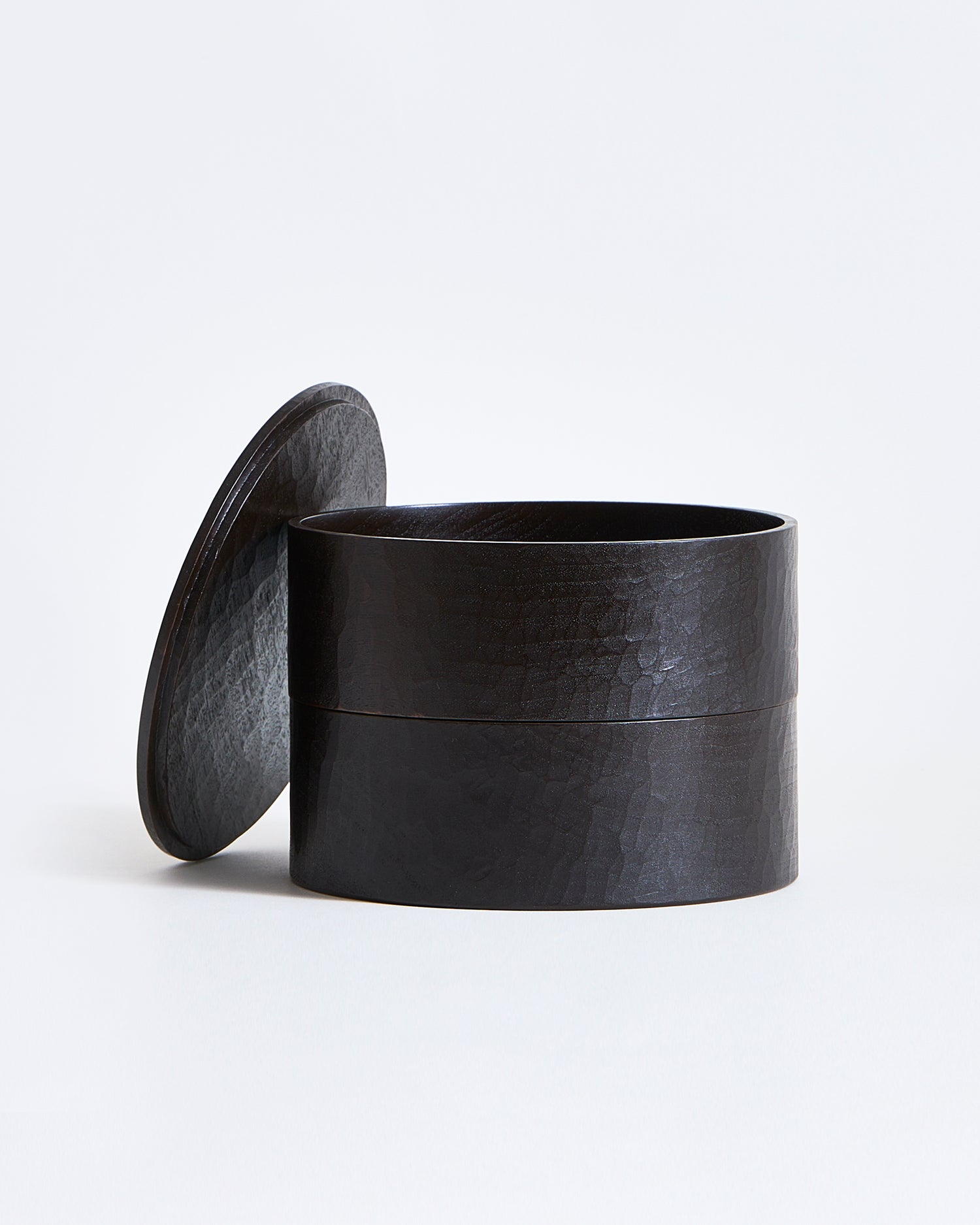 Black cylindrical two-tiered container with lid by Ryuji Mitani on a gray  background