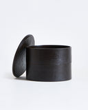 Black cylindrical two-tiered container with lid by Ryuji Mitani on a gray  background